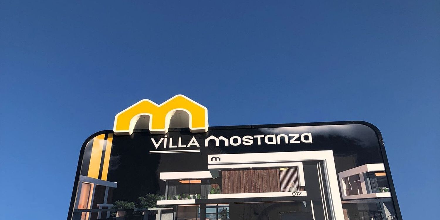 Villa Mostanza proje tabelası: sarı Mostanza işareti, proje adı ve villa görseli (fotoğraf)